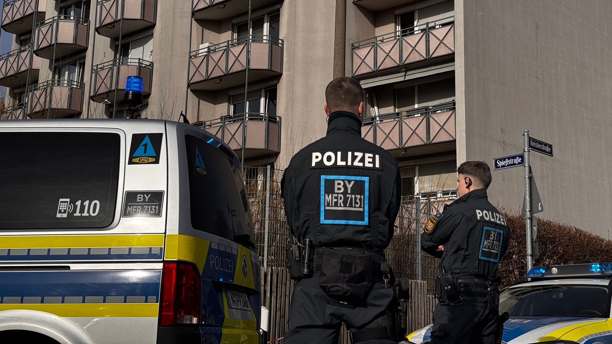 Zwei Polizisten stehen neben Einsatzfahrzeugen vor einem Wohngebäude in Nürnberg.