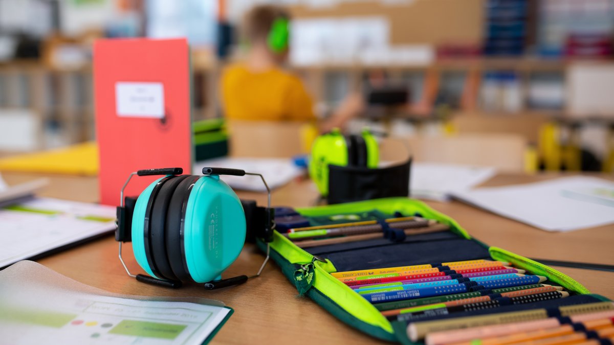 Ein Mäppchen und ein Gehörschutz liegen im Klassenzimmer einer 2. Klasse einer Grundschule auf einem Tisch (Symbolbild)