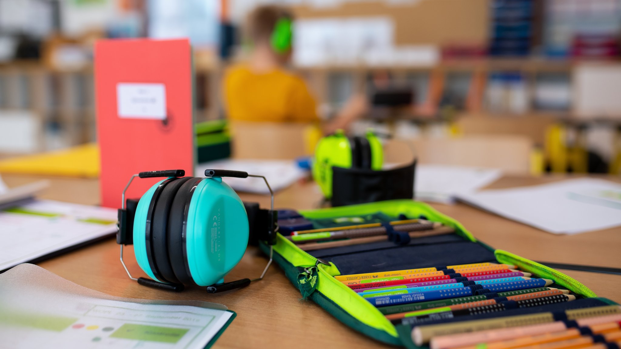 Ein Mäppchen und ein Gehörschutz liegen im Klassenzimmer einer 2. Klasse einer Grundschule auf einem Tisch (Symbolbild)