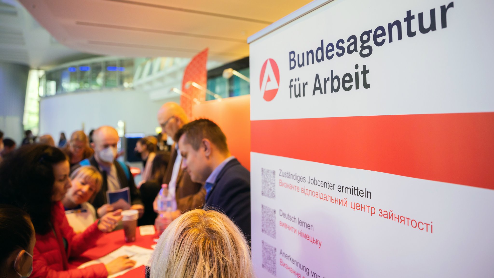 Menschen stehen bei einer Jobmesse für ukrainische Geflüchtete von der IHK Berlin und der Agentur für Arbeit am Stand der Bundesagentur für Arbeit.