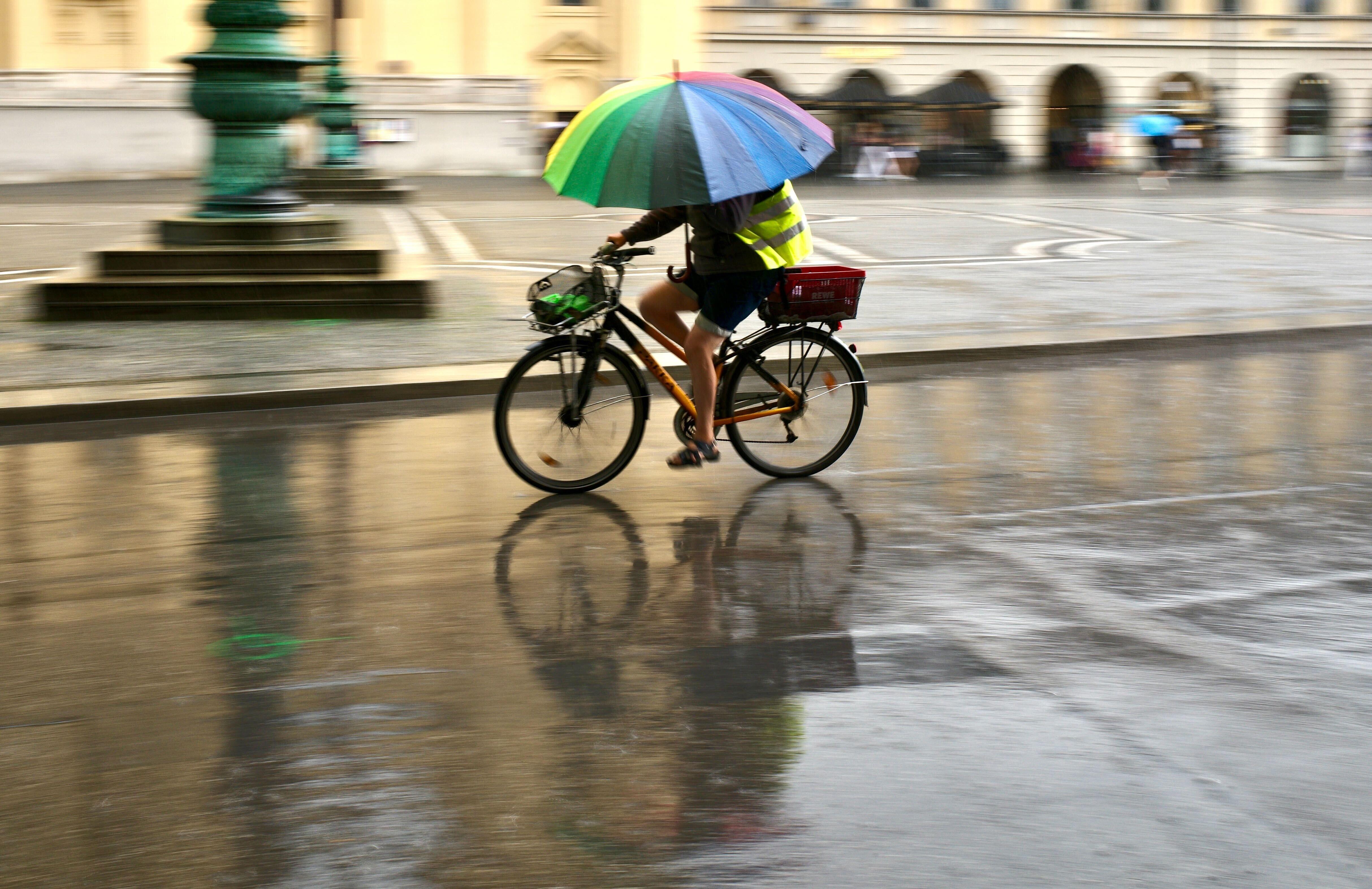 Symbolfoto: Ein Mann fährt bei Regen mit einem bunten Schirm über den Odeonsplatz in München.