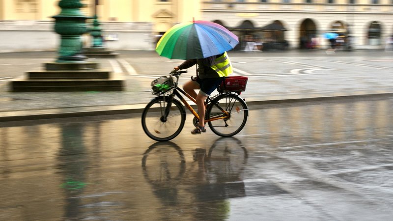 Symbolfoto: Ein Mann fährt bei Regen mit einem bunten Schirm über den Odeonsplatz in München. | Bild: picture alliance/dpa | Peter Kneffel Symbolfoto: Ein Mann fährt bei Regen mit einem bunten Schirm über den Odeonsplatz in München.