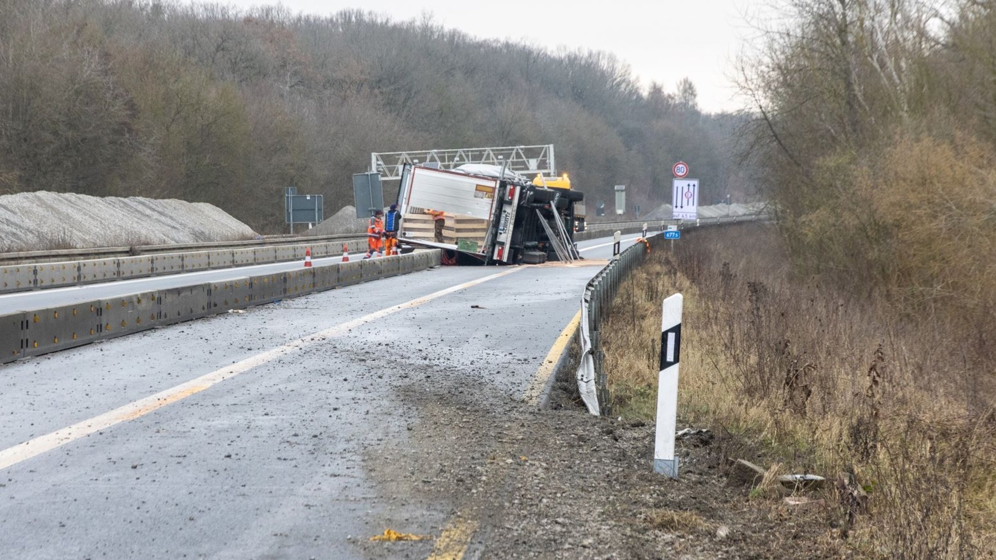 Der umgestürzte Sattelzug liegt auf der A7 Richtung Kassel und wird von Einsatzkräften inspiziert