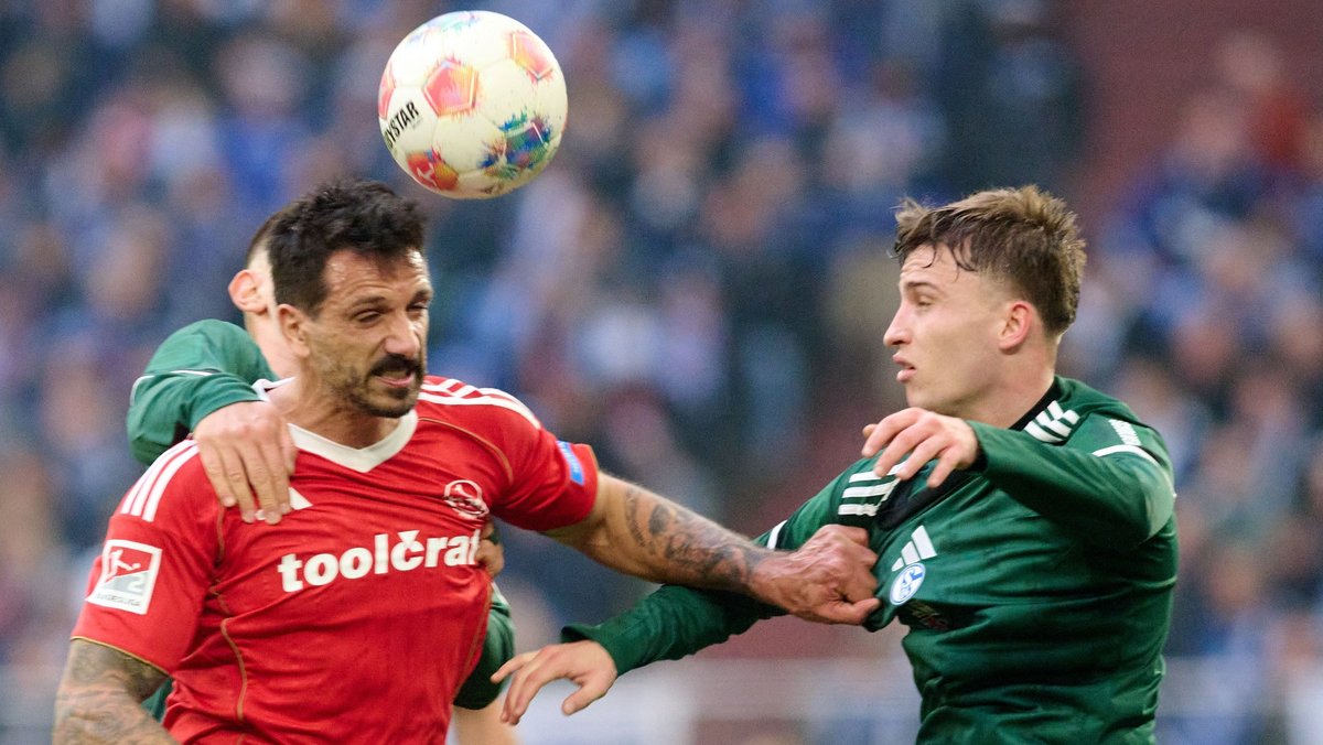 14.12.2025, Nordrhein-Westfalen, Gelsenkirchen: Fußball: 2. Bundesliga, FC Schalke 04 - 1. FC Nürnberg, 16. Spieltag, Veltins Arena. Adriano Grimaldi (1. FC Nürnberg, l.) und Vitalie Becker (FC Schalke 04) in Aktion. Foto: Bernd Thissen/dpa - WICHTIGER HINWEIS: Gemäß den Vorgaben der DFL Deutsche Fußball Liga bzw. des DFB Deutscher Fußball-Bund ist es untersagt, in dem Stadion und/oder vom Spiel angefertigte Fotoaufnahmen in Form von Sequenzbildern und/oder videoähnlichen Fotostrecken zu verwerten bzw. verwerten zu lassen. +++ dpa-Bildfunk +++