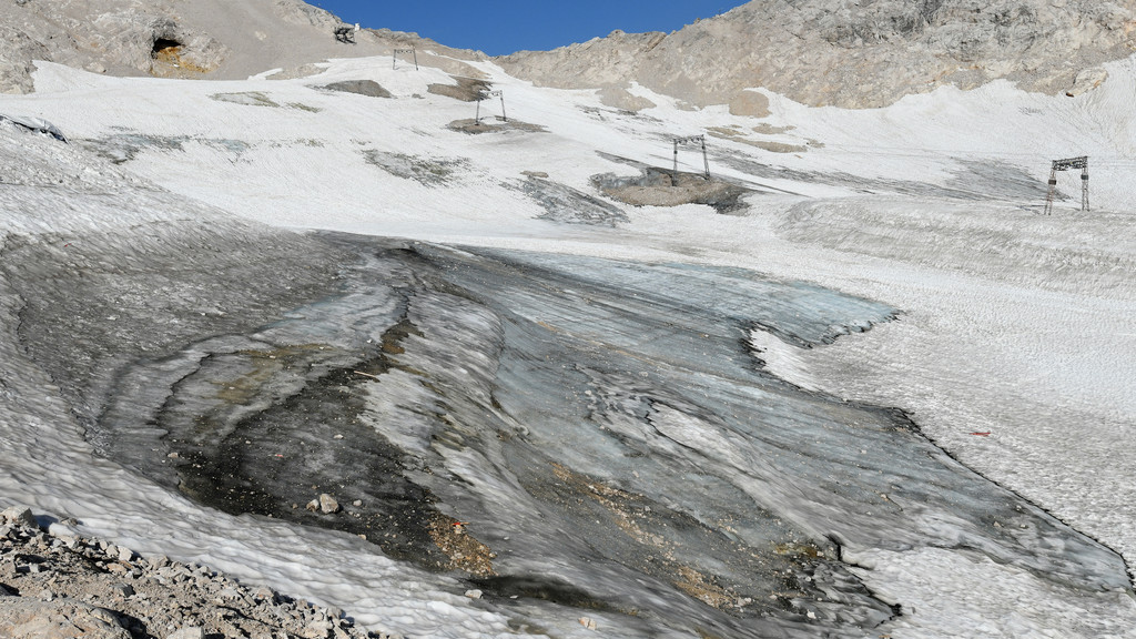 Schneereste auf felsigem Untergrund - vorne  schwarzgrauer Gletscher, dahinter Liftstützen des Skigebiets auf der Zugspitze