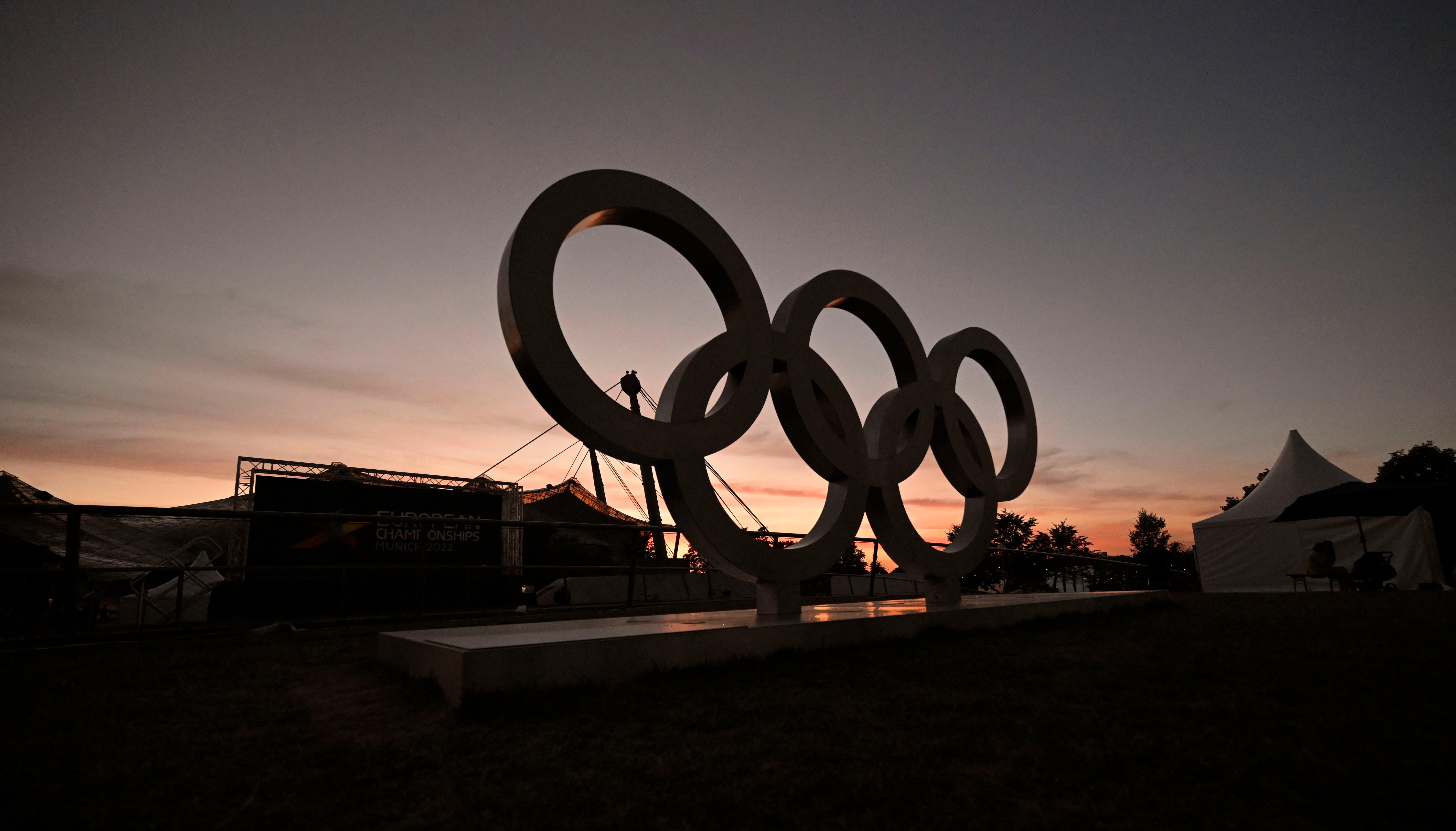 Die olympischen Ringe stehen 2022 während der European Championships in München im Olympiapark. Im Hintergrund sieht man die Sportstätten und einen Sonnenuntergang