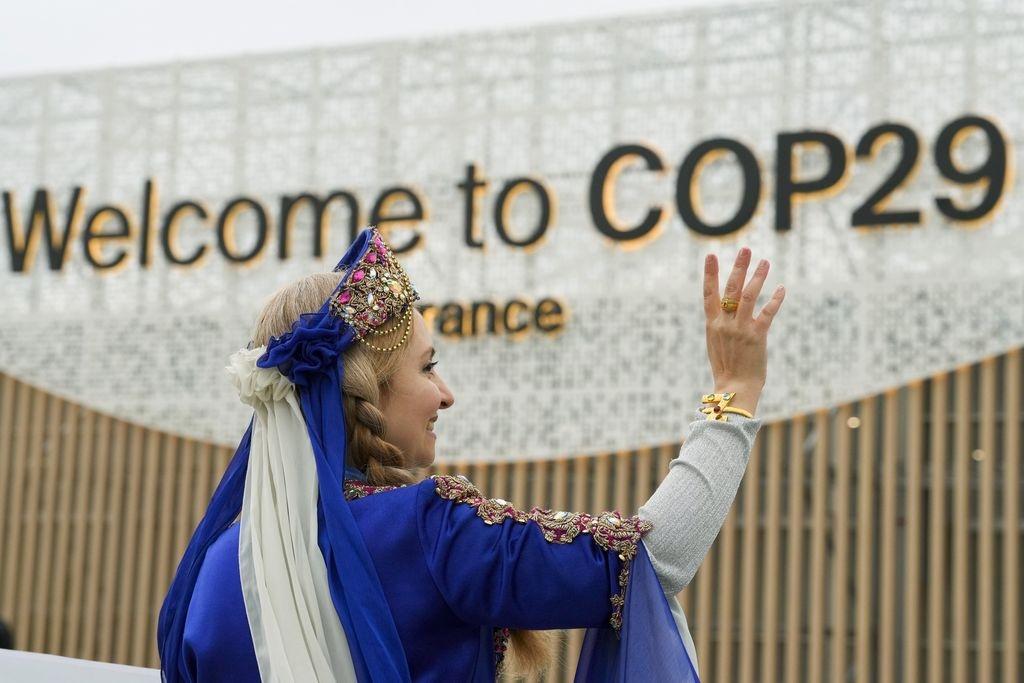 dpatopbilder - 12.11.2024, Aserbaidschan, Baku: Eine Frau in Tracht winkt vor dem Eingang zum Tagungsort des UN-Klimagipfels COP29. Foto: Peter Dejong/AP/dpa +++ dpa-Bildfunk +++