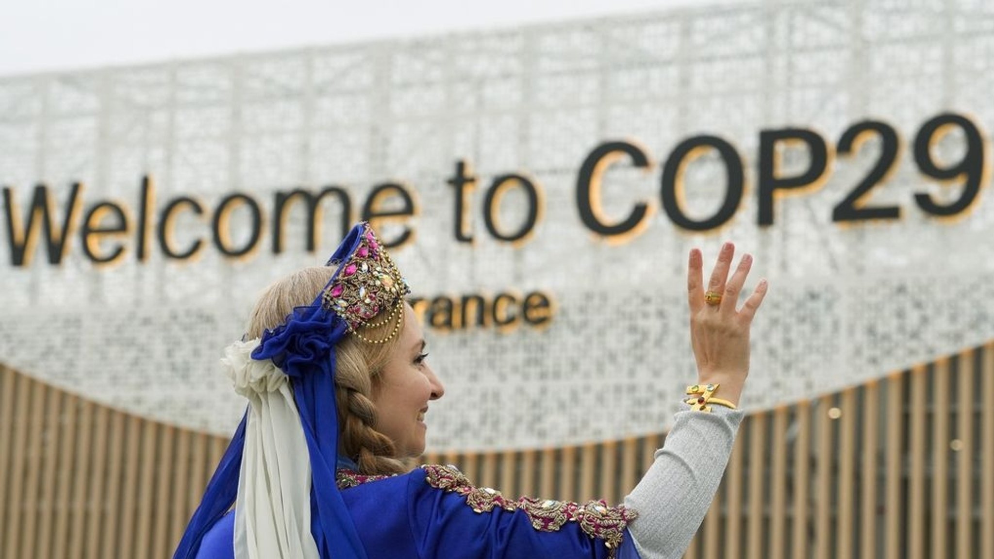 dpatopbilder - 12.11.2024, Aserbaidschan, Baku: Eine Frau in Tracht winkt vor dem Eingang zum Tagungsort des UN-Klimagipfels COP29. Foto: Peter Dejong/AP/dpa +++ dpa-Bildfunk +++