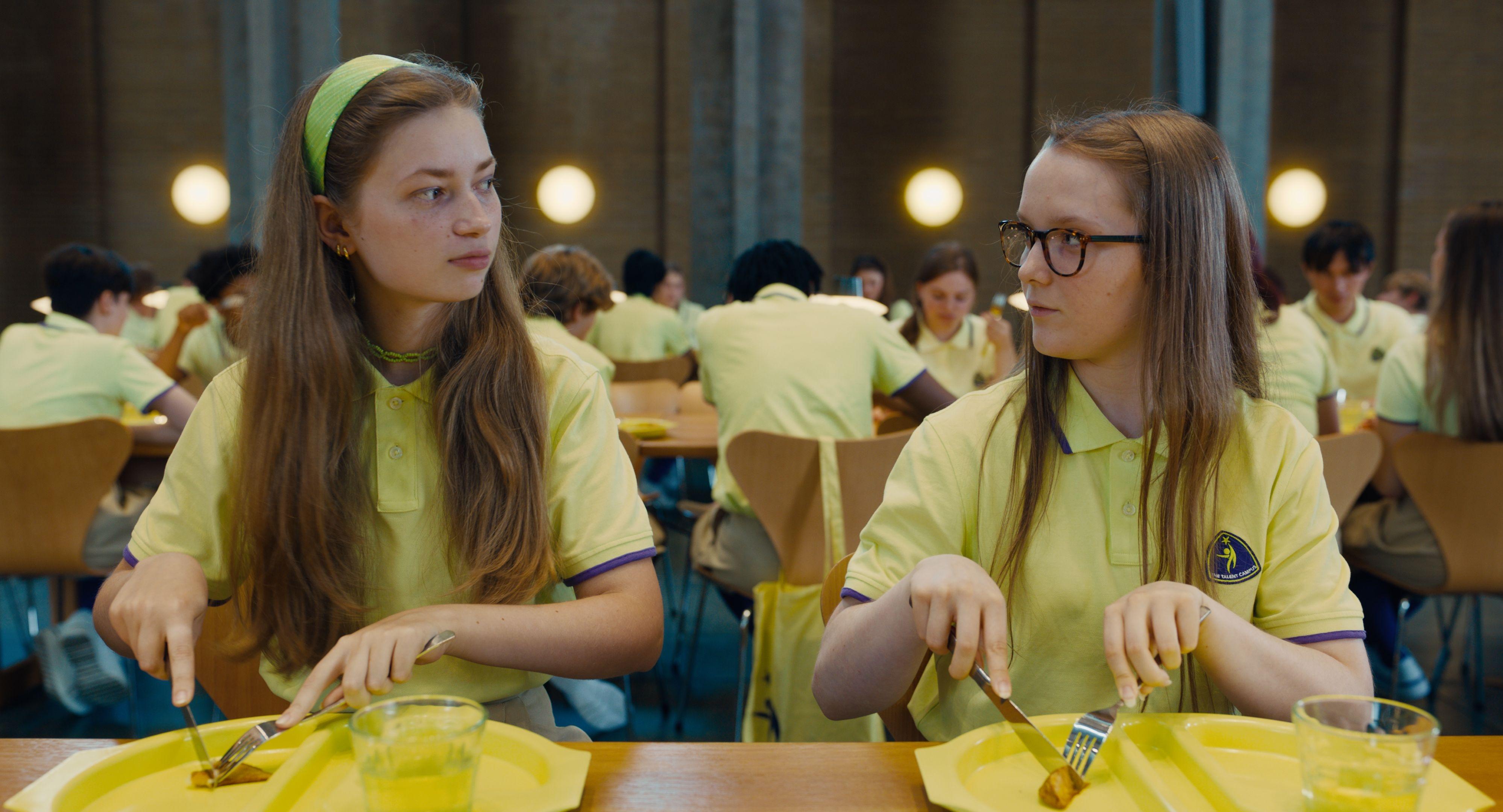 Zwei Internats-Schülerinnen beim Essen in der Mensa sehen sich kritisch an.