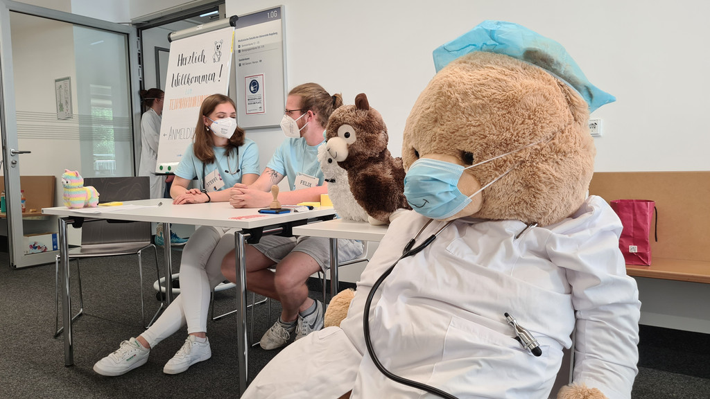 Das Bild zeigt einen großen Teddybären und Medizinstudenten der Uni Augsburg.