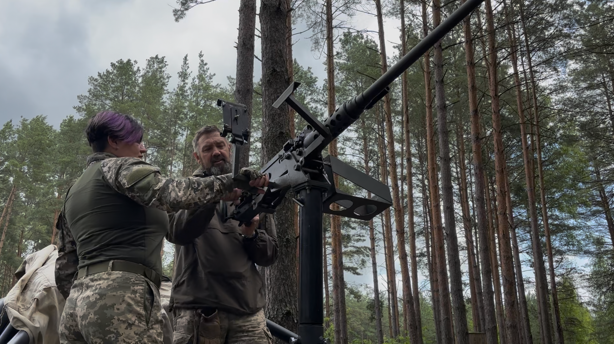 Ein Mann und eine Frau stehen im Wald und bedienen ein Gewehr.