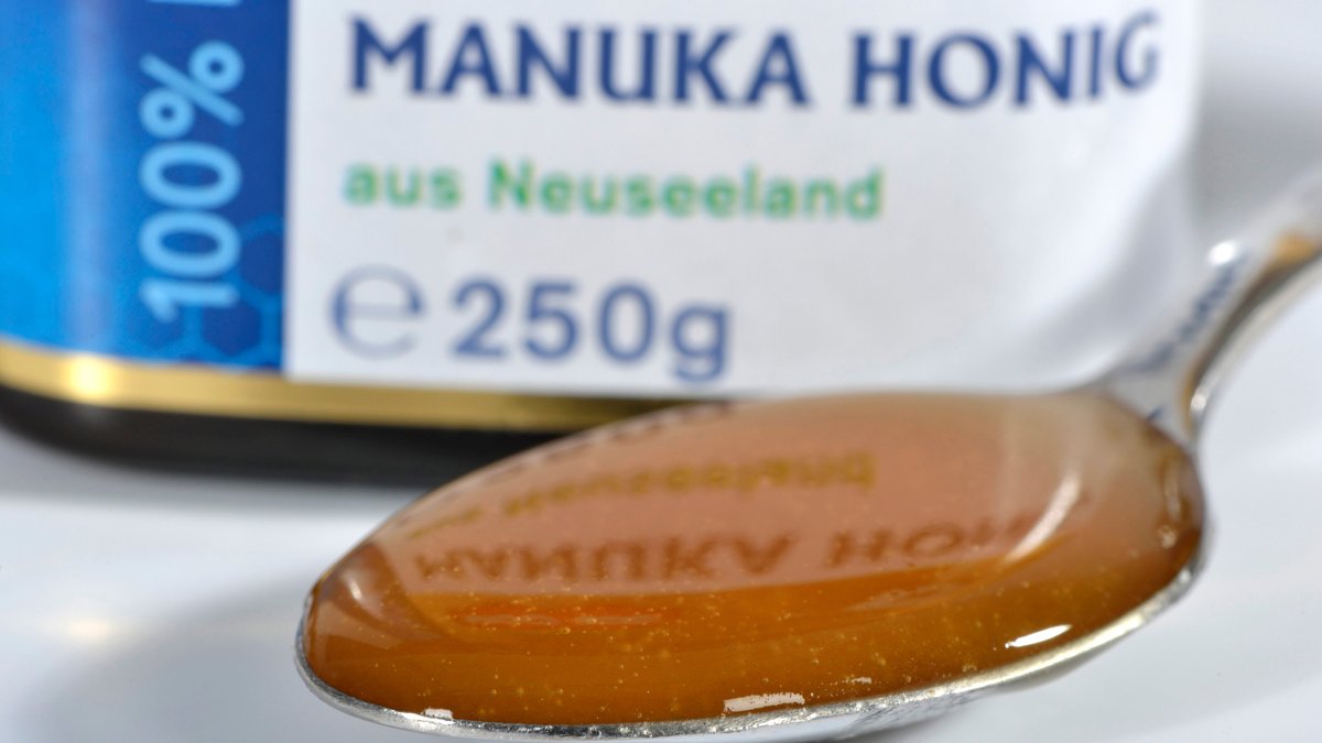 Ein Glas Manuka Honig im Hintergrund. Im Vordergrund ein Löffel mit Honig.