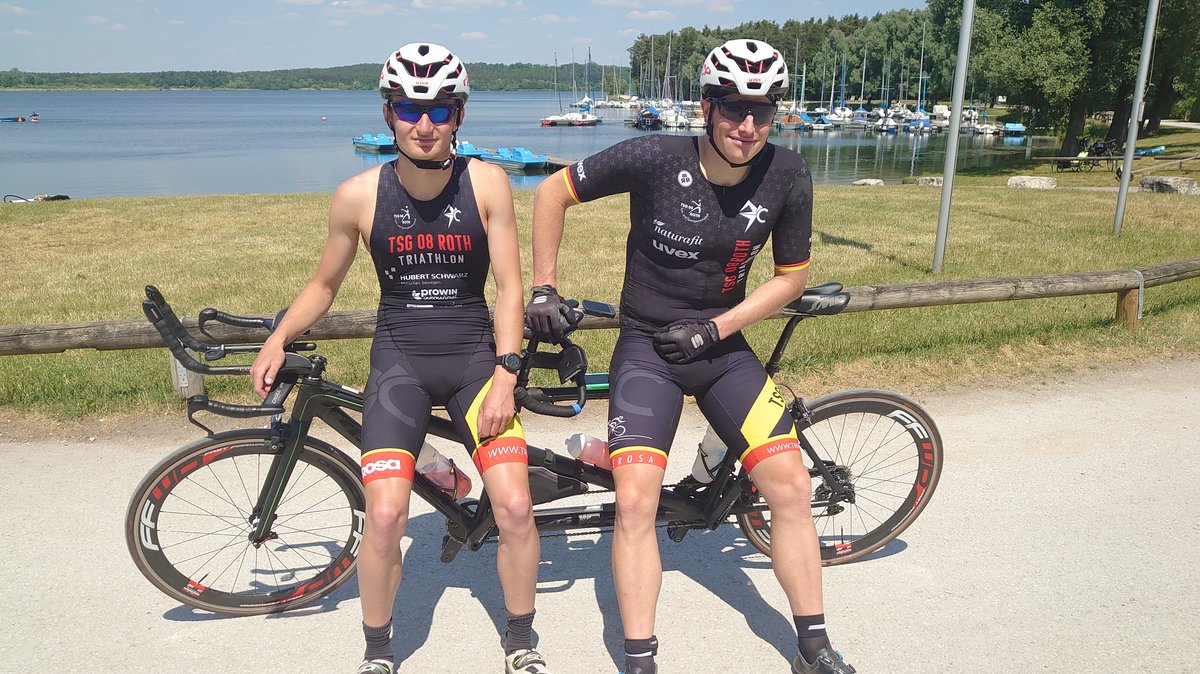 Der blinde Tim Kleinwächter und sein Rad-Pilot Raphael Junghans stehen nebeneinander angelehnt an ihr Tandemrad.