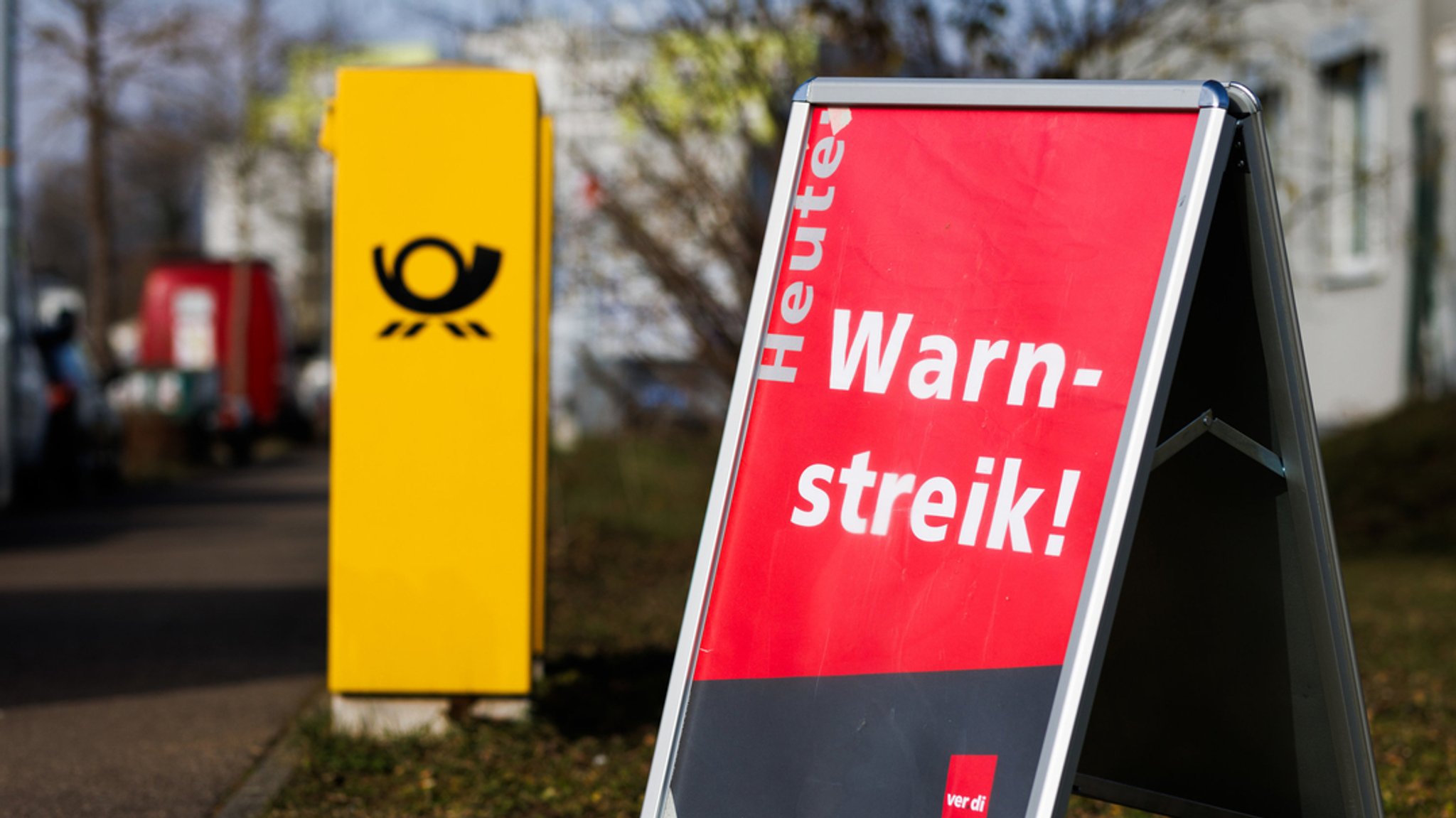 Ein Aufsteller mit der Aufschrift "Heute Warnstreik!" steht neben einem Briefkasten der Deutschen Post.