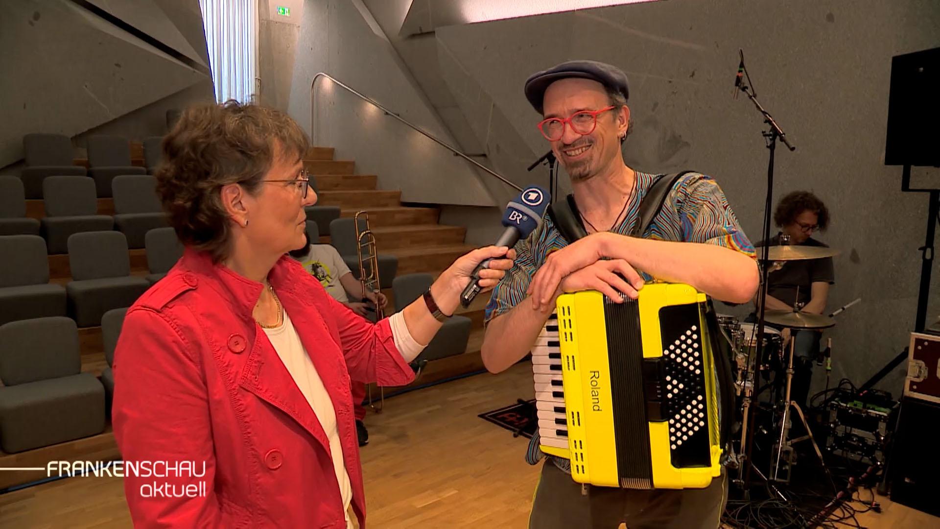 Eine Reporterin interviewt einen Akkordeon-Spieler.