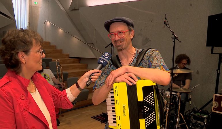 Eine Reporterin interviewt einen Akkordeon-Spieler. | Bild: BR 2024 Eine Reporterin interviewt einen Akkordeon-Spieler.