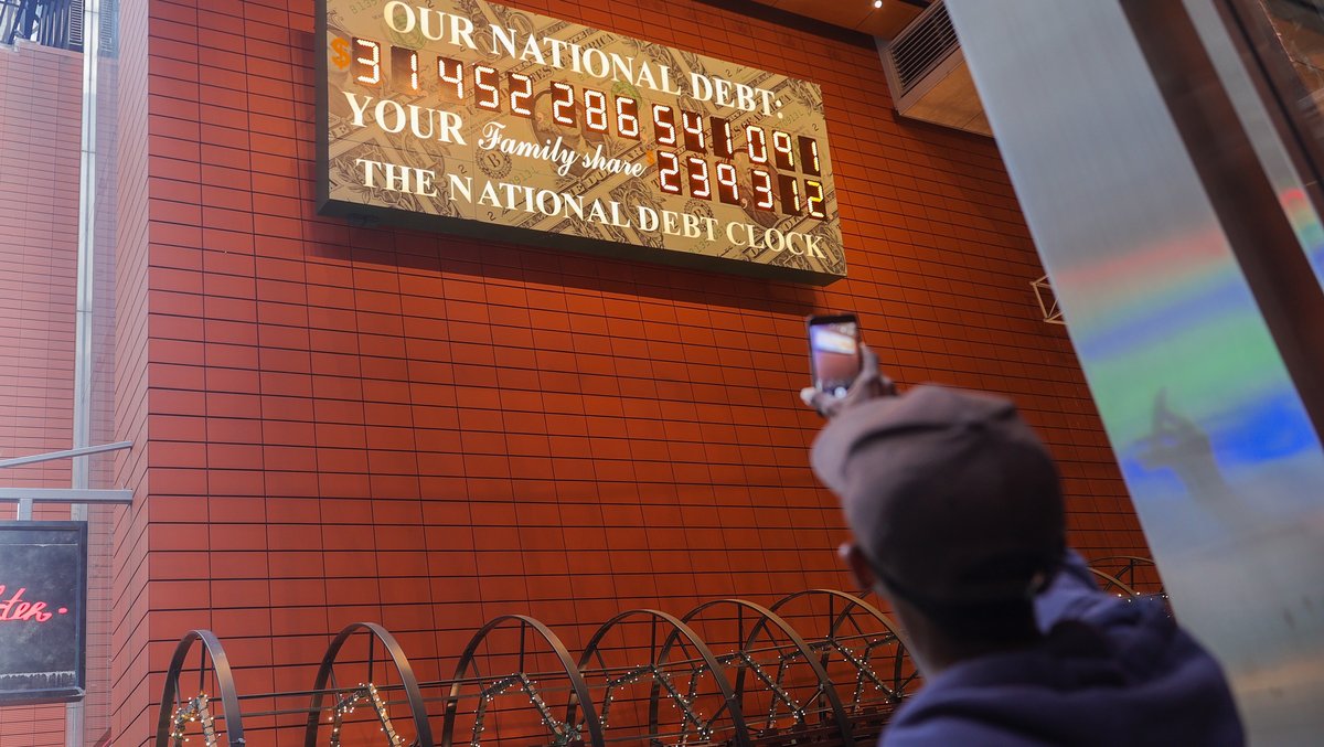 Mann fotografiert mit dem Handy die  "Schuldenuhr"in Manhattan, ein Display, das die aktuellen US-Schulden zeigt