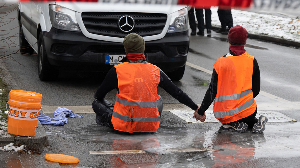 Zwei Klimaaktivisten nehmen an einer Protestaktion der Gruppe "Letzte Generation" teil, indem sie trotz Regen versuchen, sich auf einer Straße festzukleben.