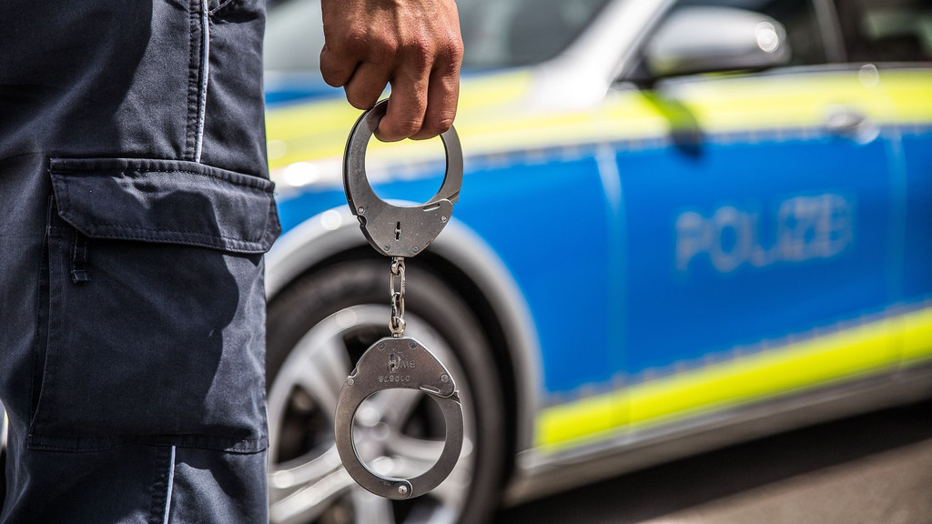 Polizist mit Handschellen vor Polizeiauto (Symbolbild)