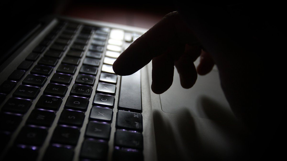 Eine Hand schwebt über einer spärlich beleuchteten Tastatur eines Laptops