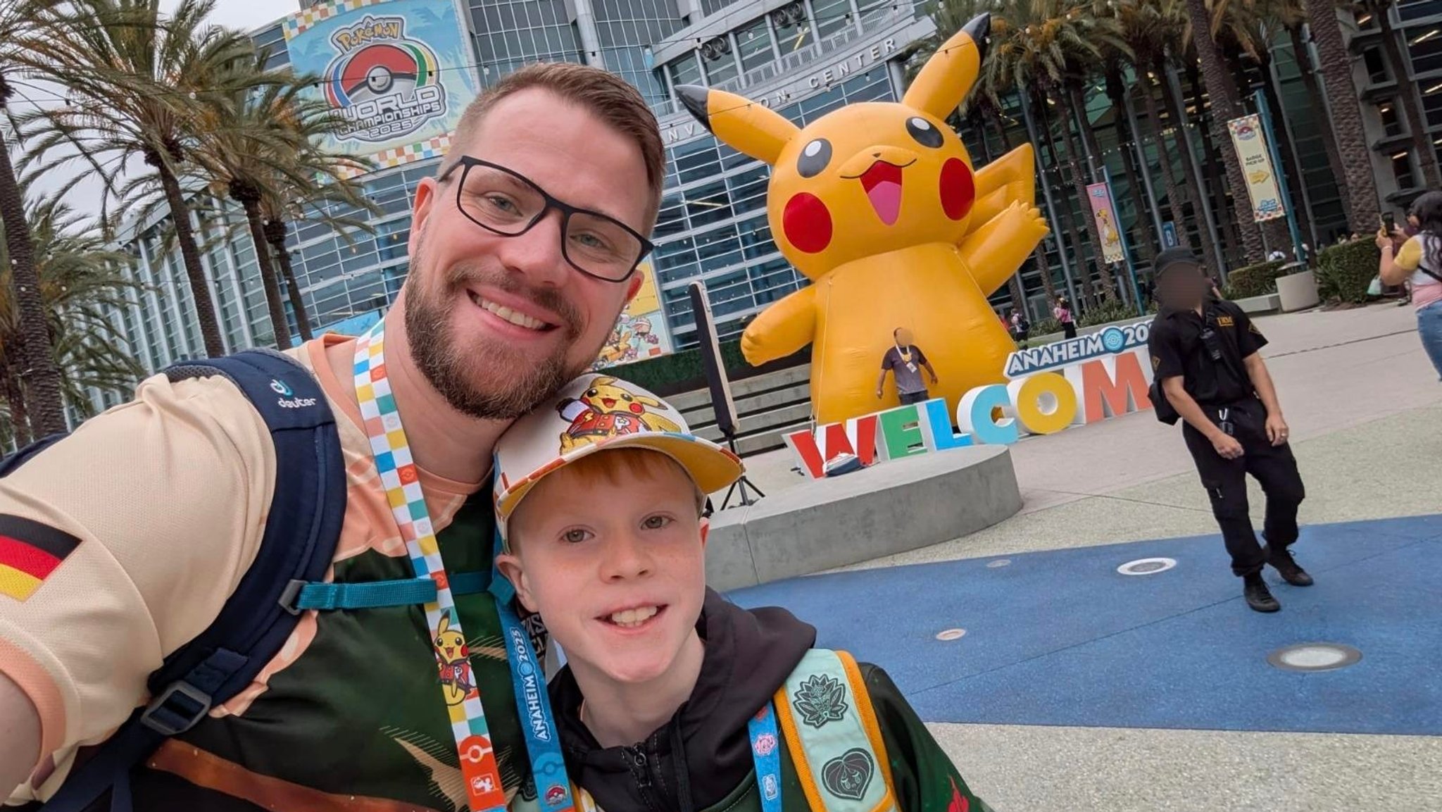 Der zehnjährige Arne Schetters mit seinem Vater Erik stehen vor dem Anaheim Convention Center, in dem die Pokémon-WM stattfindet, und lächeln in die Kamera. Im Hintergrund lächelt ein riesiges aufblasbares Pikachu. | Bild: Erik Schetters Der zehnjährige Arne Schetters mit seinem Vater Erik stehen vor dem Anaheim Convention Center, in dem die Pokémon-WM stattfindet, und lächeln in die Kamera. Im Hintergrund lächelt ein riesiges aufblasbares Pikachu.