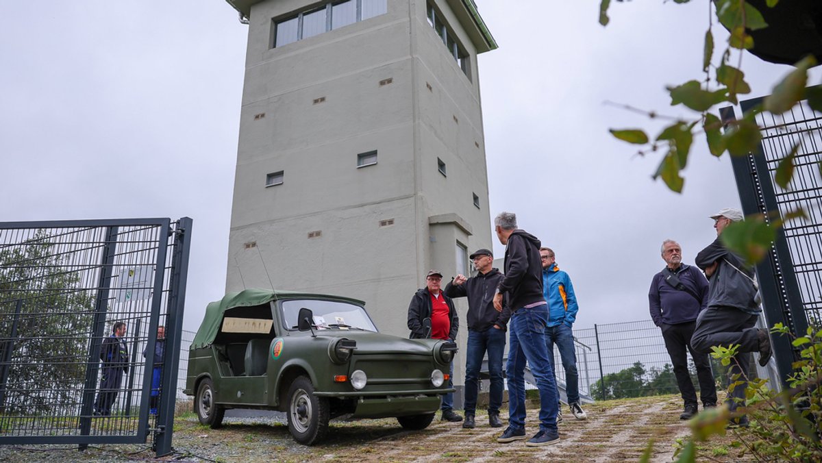 Gäste stehen zur Eröffnung des frisch sanierten Grenzturms Heinersgrün im Vogtland um einen Trabant Kübel der früheren Nationalen Volksarmee (NVA).