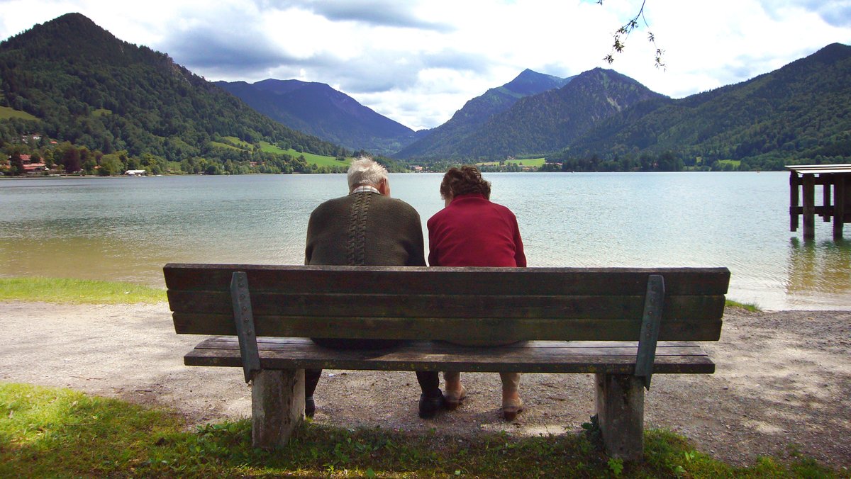Ein Rentner-Paar sitzt an einem See.