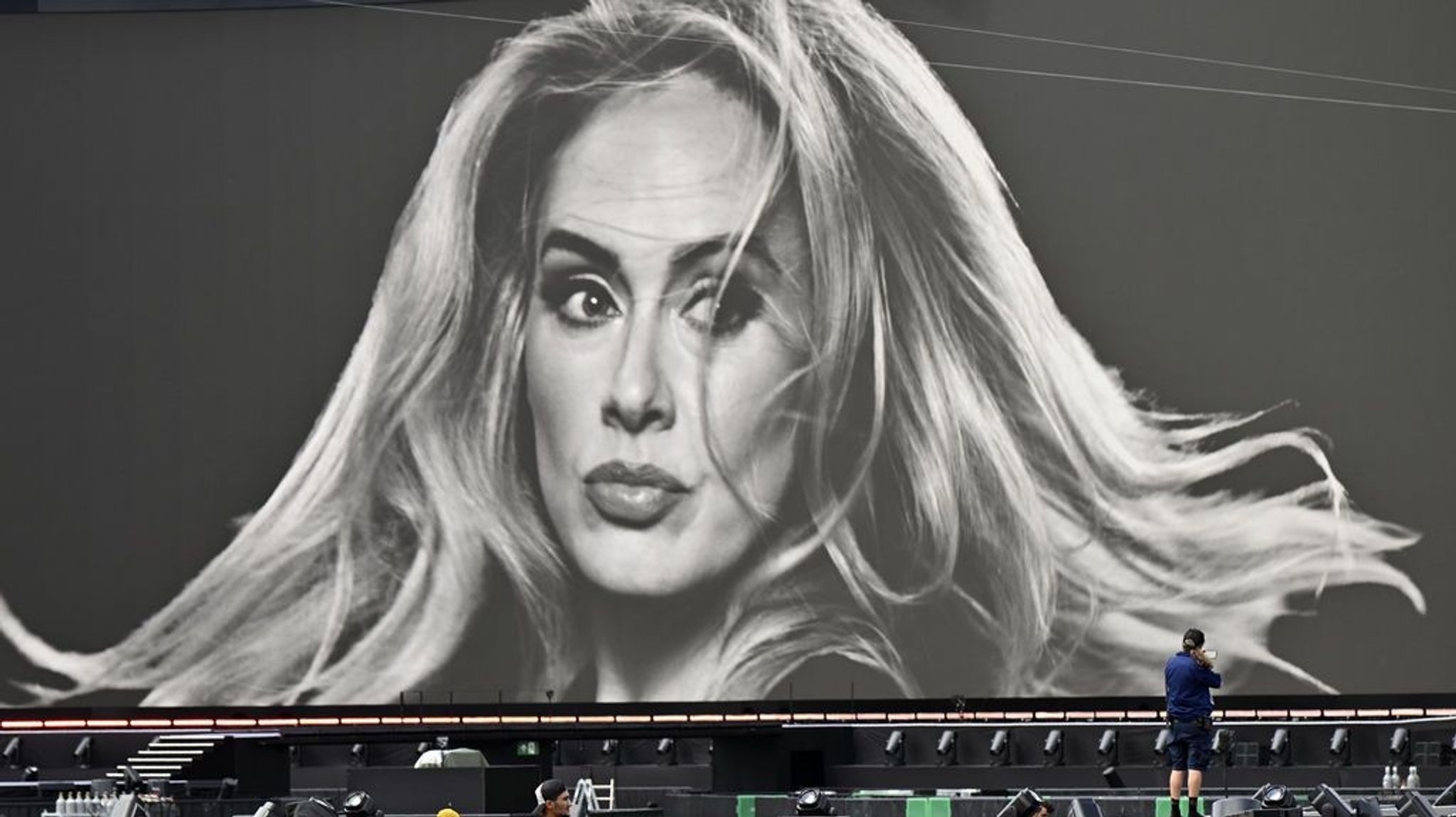 Ein Veranstaltungstechniker vor einer großen Leinwand mit einem Porträt der Sängerin Adele in der Adele World in München.