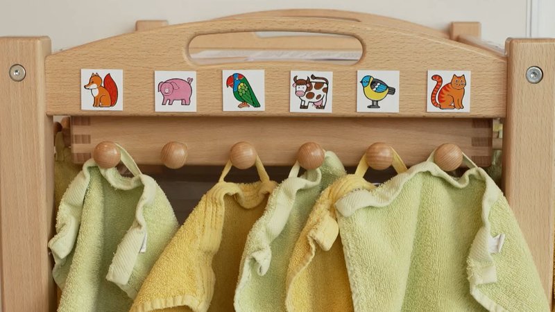 Handtücher hängen in einer Kita an Haken mit Bildern.