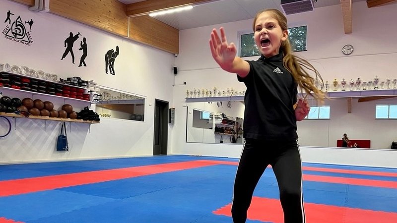 Ein 11-jähriges Mädchen in schwarzen Trainingsklamotten schlägt mit der flachen Hand vor sich in die Luft, das Gesicht zu einem Schrei verzerrt.