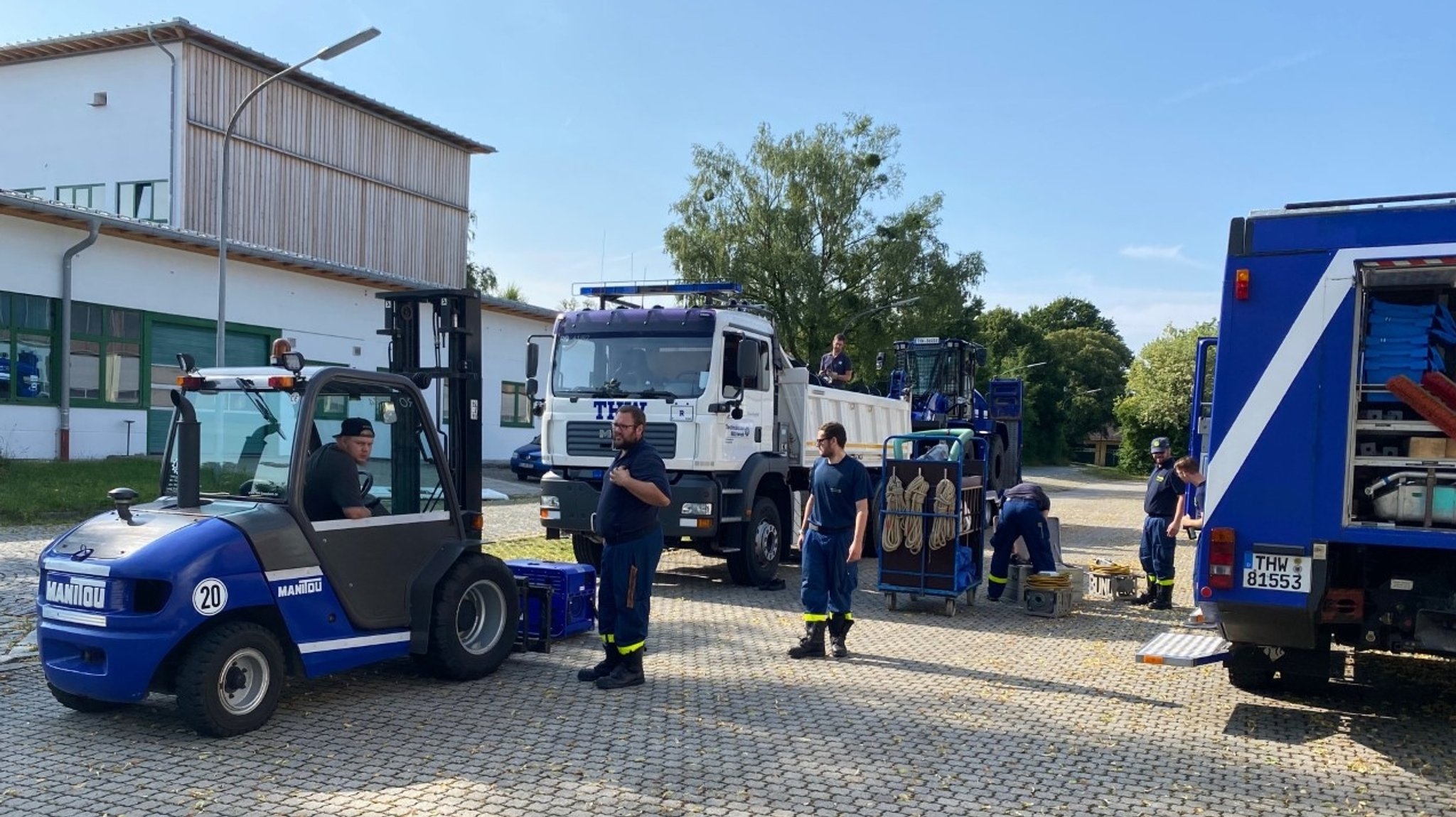 Fahrzeuge des THW Rosenheim stehen auf einem Platz. Helfer räumen die Fahrzeuge ein.