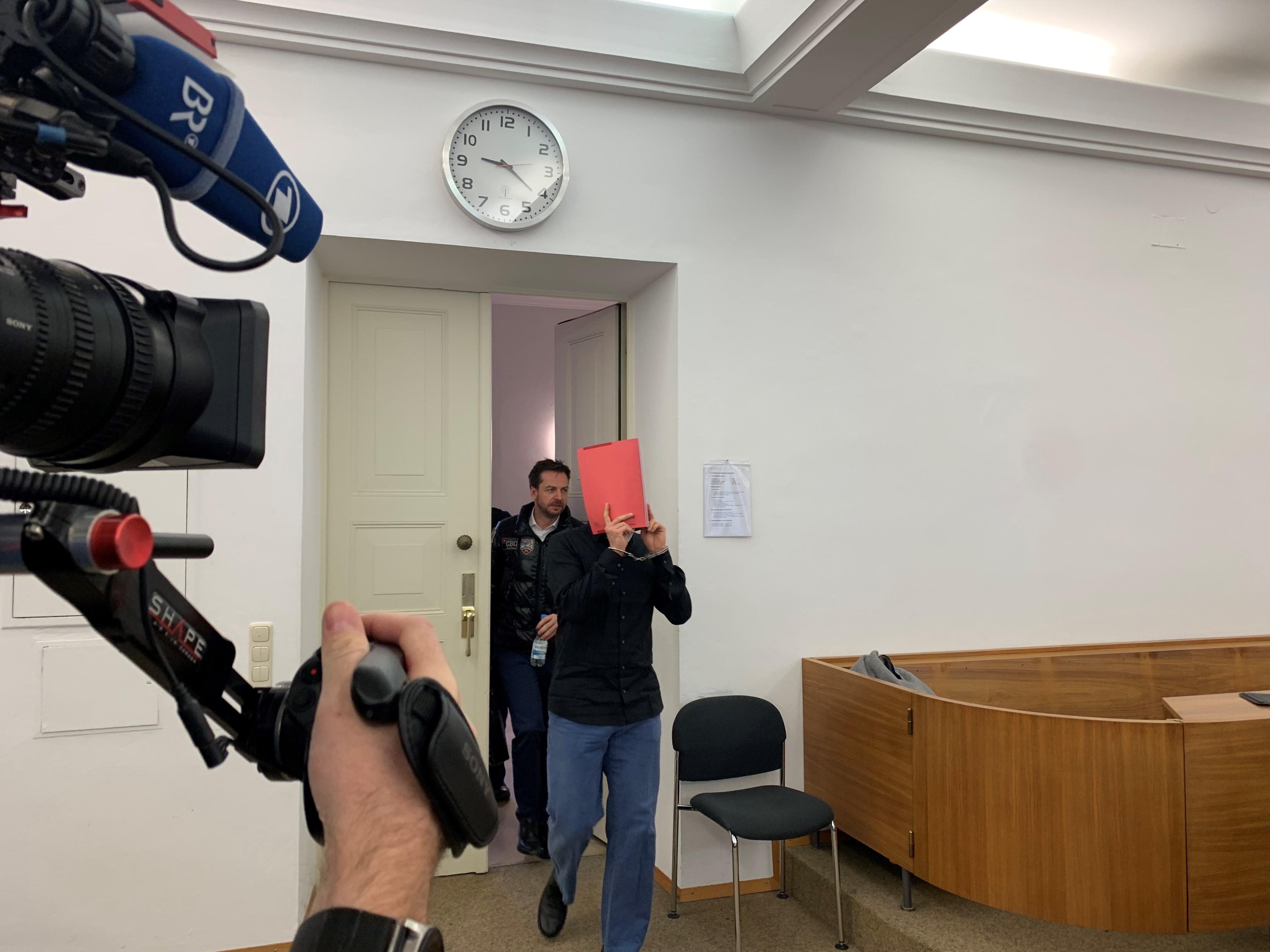 Der Angeklagte im Mordprozess nach der Gewalttat bei Schloss Neuschwanstein. Er verbirgt sein Gesicht hinter einem roten Schnellhefter.