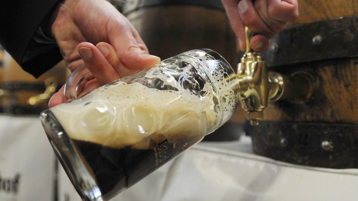 Aus einem Fass wird dunkles Bier in einen Glaskrug abgezapft.