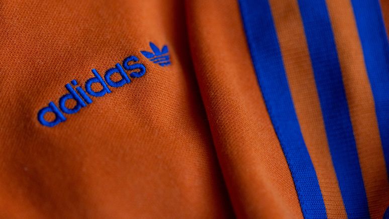 Das Logo des Sportartikelherstellers adidas in blau auf einer orangen Jacke | Bild:dpa-Bildfunk/Daniel Karmann