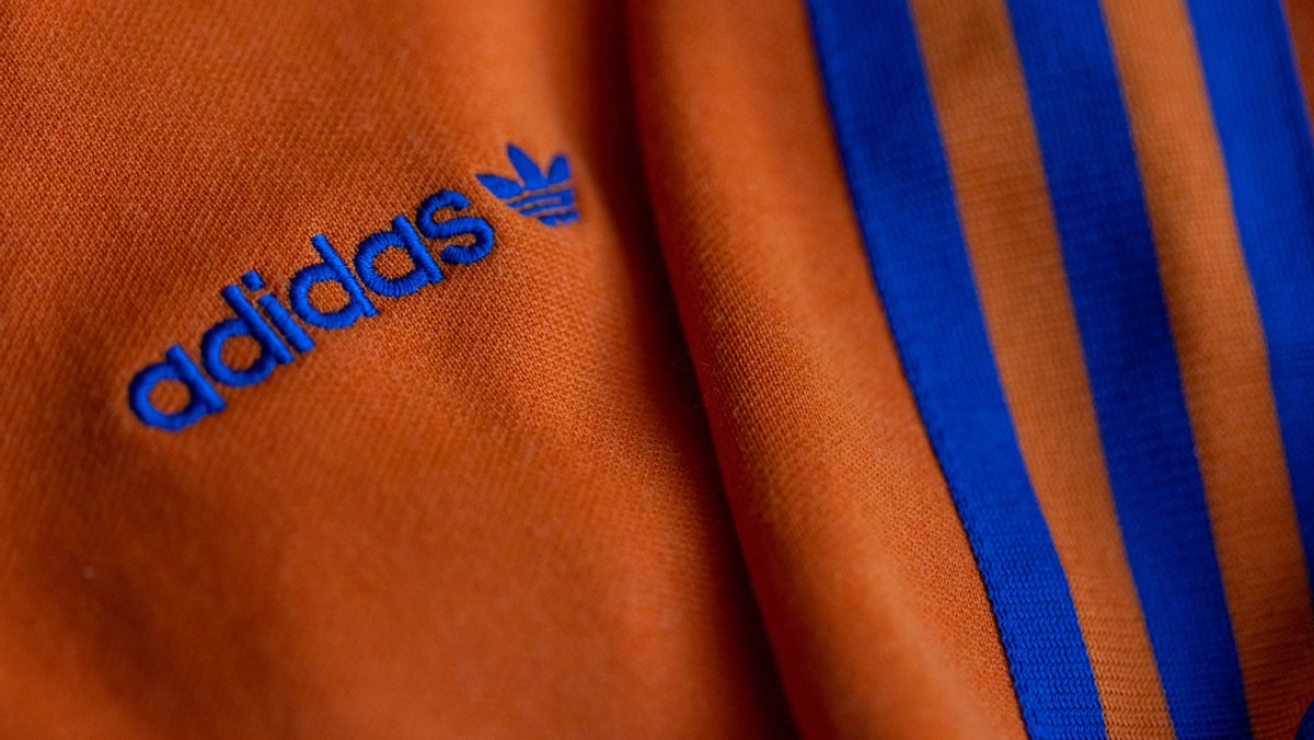 Das Logo des Sportartikelherstellers adidas in blau auf einer orangen Jacke