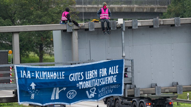 Klimaaktivisten demonstrieren mit einem Plakat auf der A9 nahe der Allianz Arena gegen die IAA. | Bild: dpa-Bildfunk/Peter Kneffel Klimaaktivisten demonstrieren mit einem Plakat auf der A9 nahe der Allianz Arena gegen die IAA.