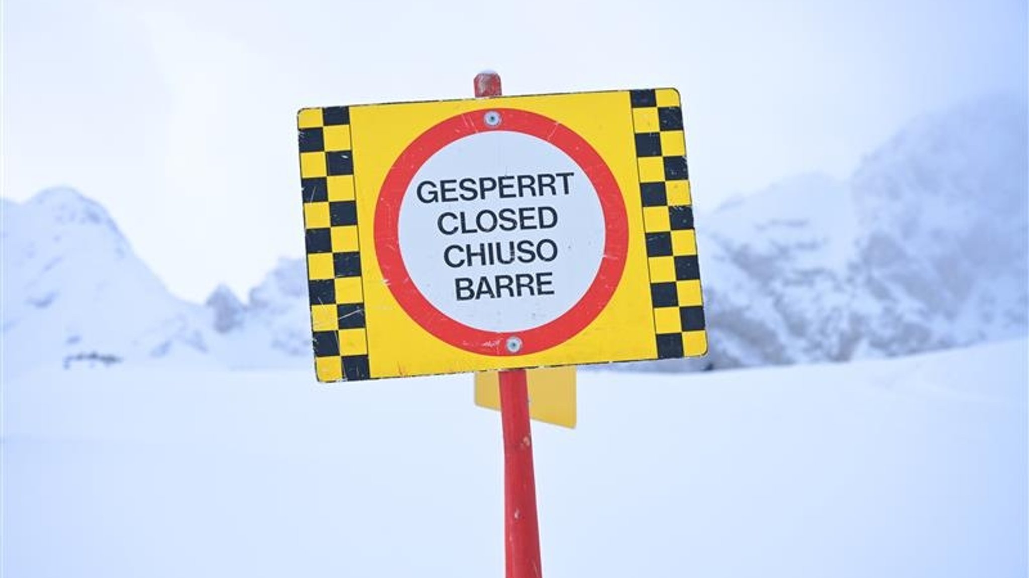 Ein Schild mit der Aufschrift "Gesperrt" in mehreren verschiedenen Sprachen steht auf der verschneiten Alpspitze. 