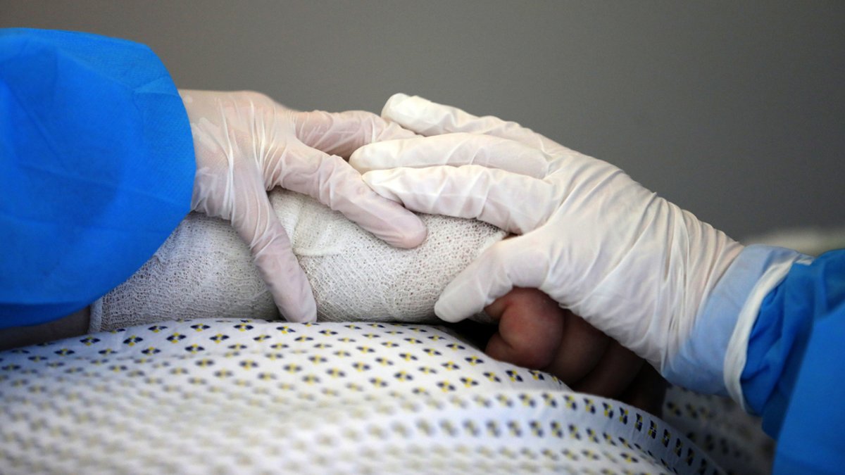Zwei Hände halten die Hand eines Patienten, der wegen Covid-19 auf einer Intensivstation liegt.