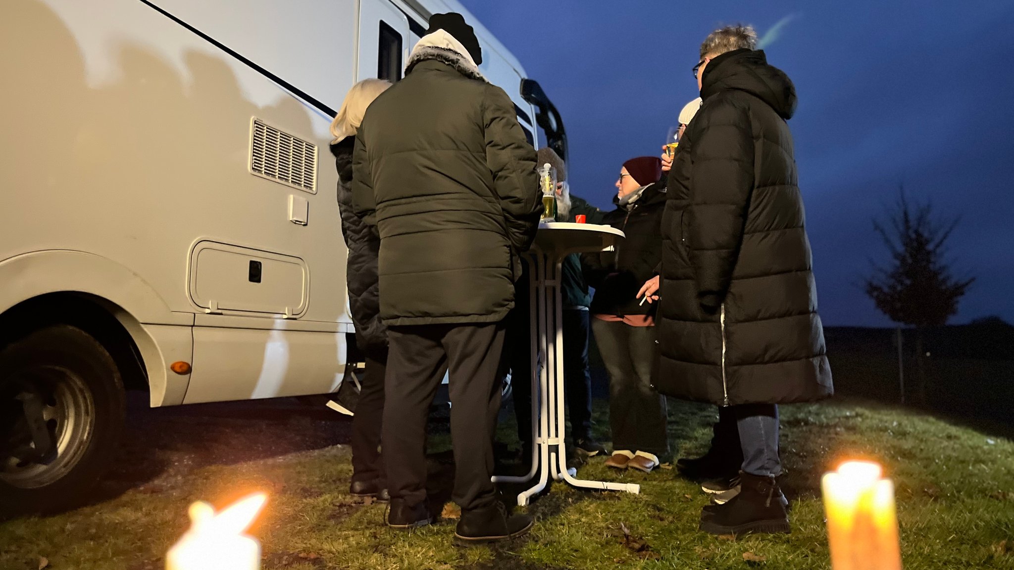 Menschen stehen in dicken Jacken rund um einen Stehtisch neben einem Wohnmobil. | Bild: BR / Valentin Beige Menschen stehen in dicken Jacken rund um einen Stehtisch neben einem Wohnmobil.