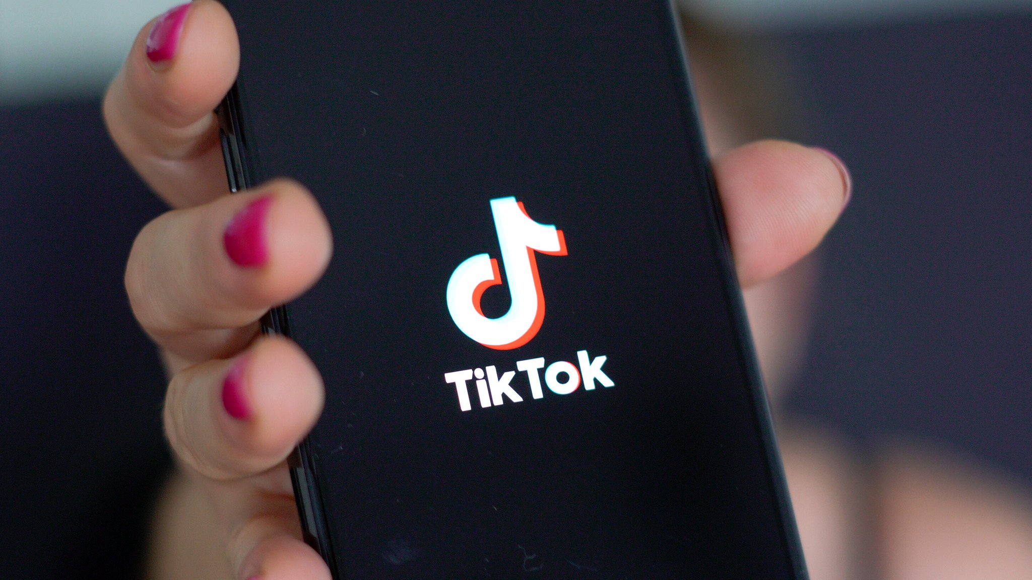 Frau hält Smartphone mit TikTok-Logo in die Kamera