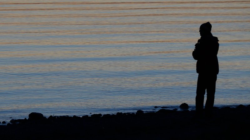 Ein Mann steht am Abend am Ufer eines Sees (Symbolbild).