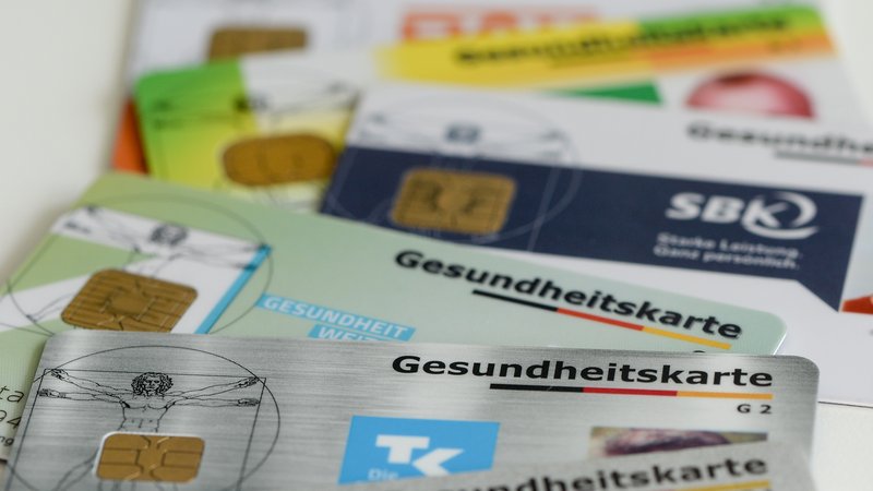 Gesundheitskarten verschiedener Krankenkassen liegen auf einem Tisch. | Bild: picture alliance / Jens Kalaene/dpa-Zentralbild/dpa | Jens Kalaene Gesundheitskarten verschiedener Krankenkassen liegen auf einem Tisch.