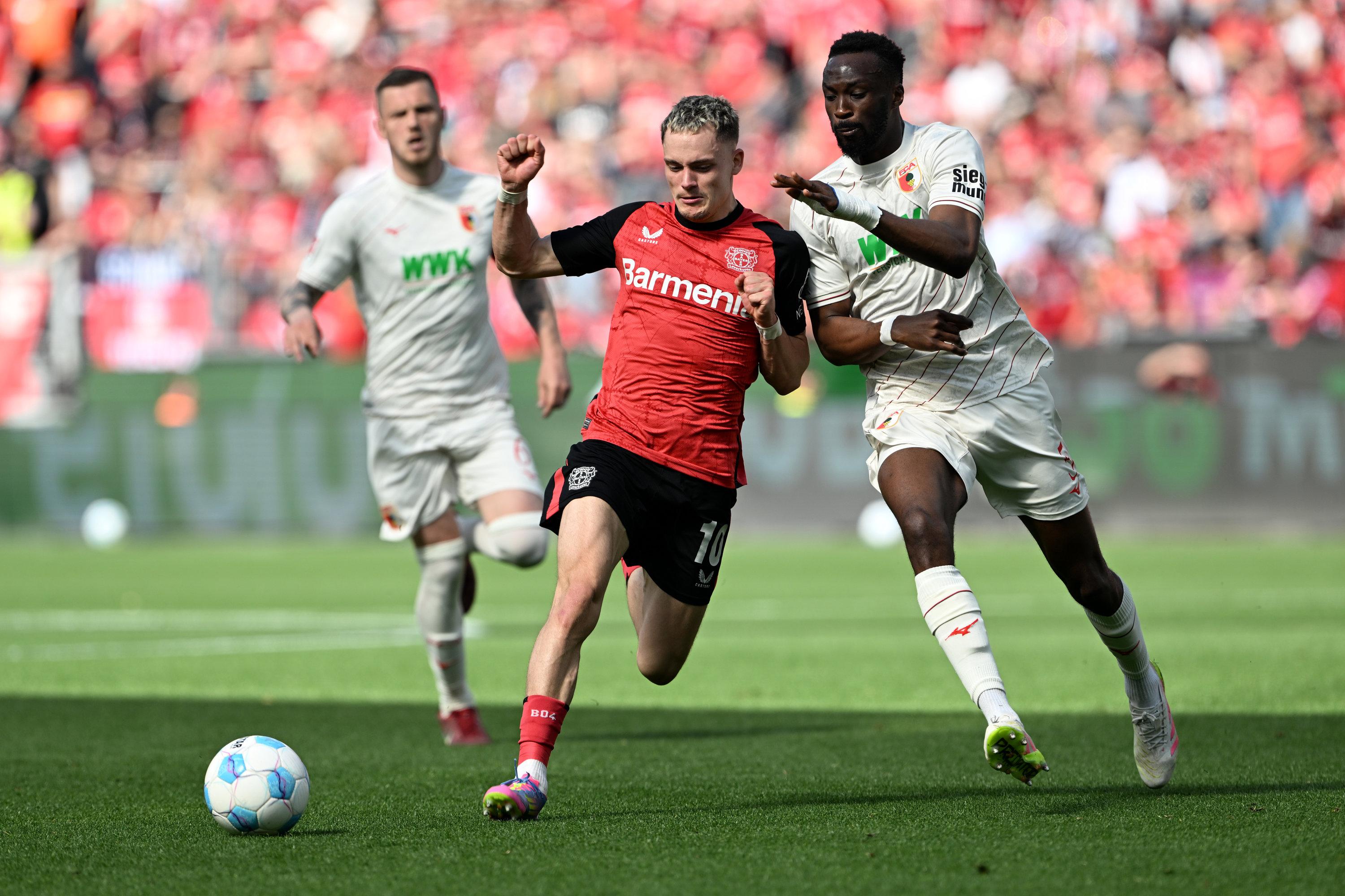 26.04.2025, Nordrhein-Westfalen, Leverkusen: Fußball: Bundesliga, Bayer Leverkusen - FC Augsburg, 31. Spieltag, BayArena, Leverkusens Florian Wirtz (l) und Augsburgs Chrislain Matsima kämpfen um den Ball. Foto: Federico Gambarini/dpa - WICHTIGER HINWEIS: Gemäß den Vorgaben der DFL Deutsche Fußball Liga bzw. des DFB Deutscher Fußball-Bund ist es untersagt, in dem Stadion und/oder vom Spiel angefertigte Fotoaufnahmen in Form von Sequenzbildern und/oder videoähnlichen Fotostrecken zu verwerten bzw. verwerten zu lassen. +++ dpa-Bildfunk +++