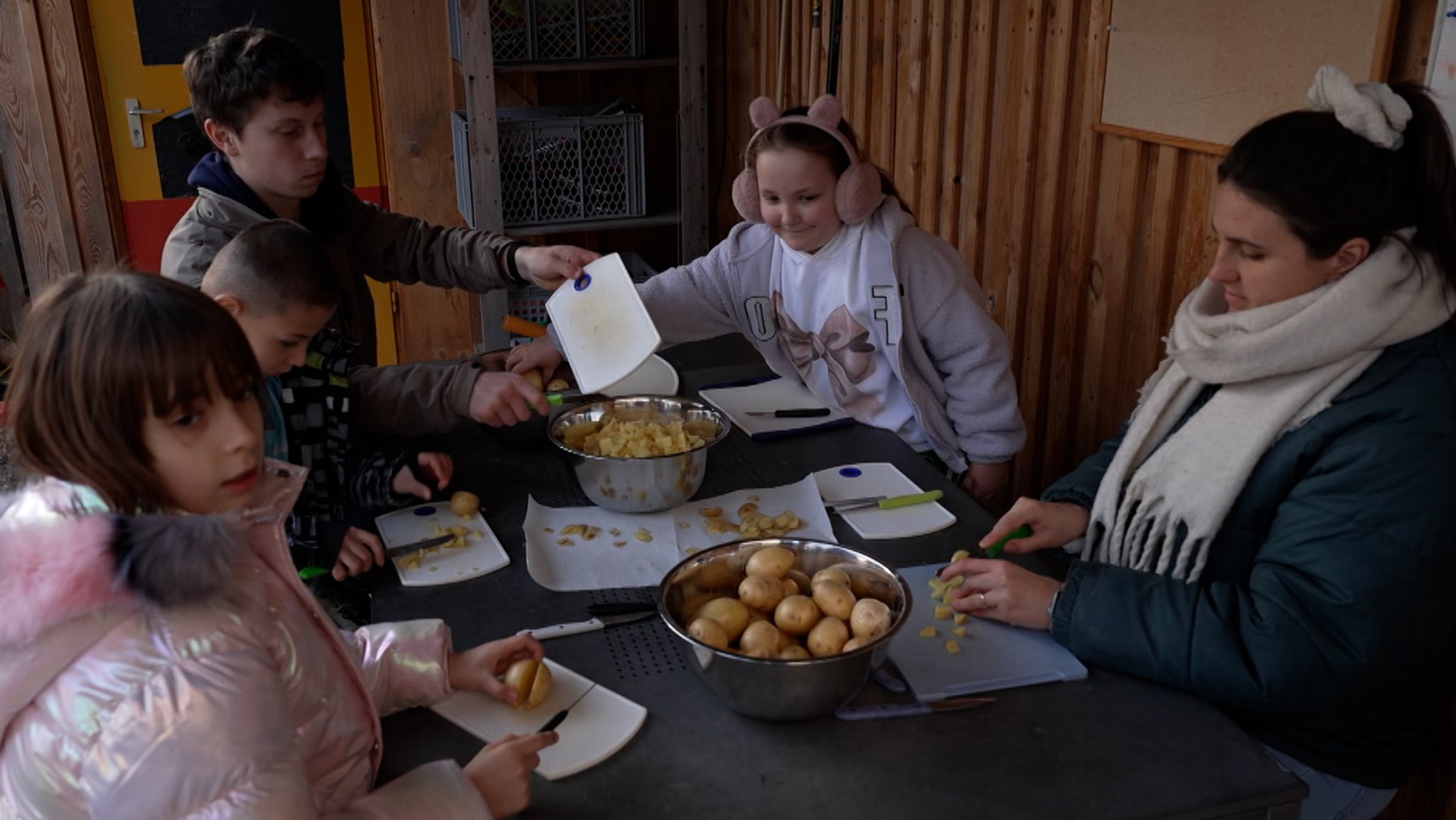 Eine Betreuerin schält zusammen mit Kindern Kartoffeln.