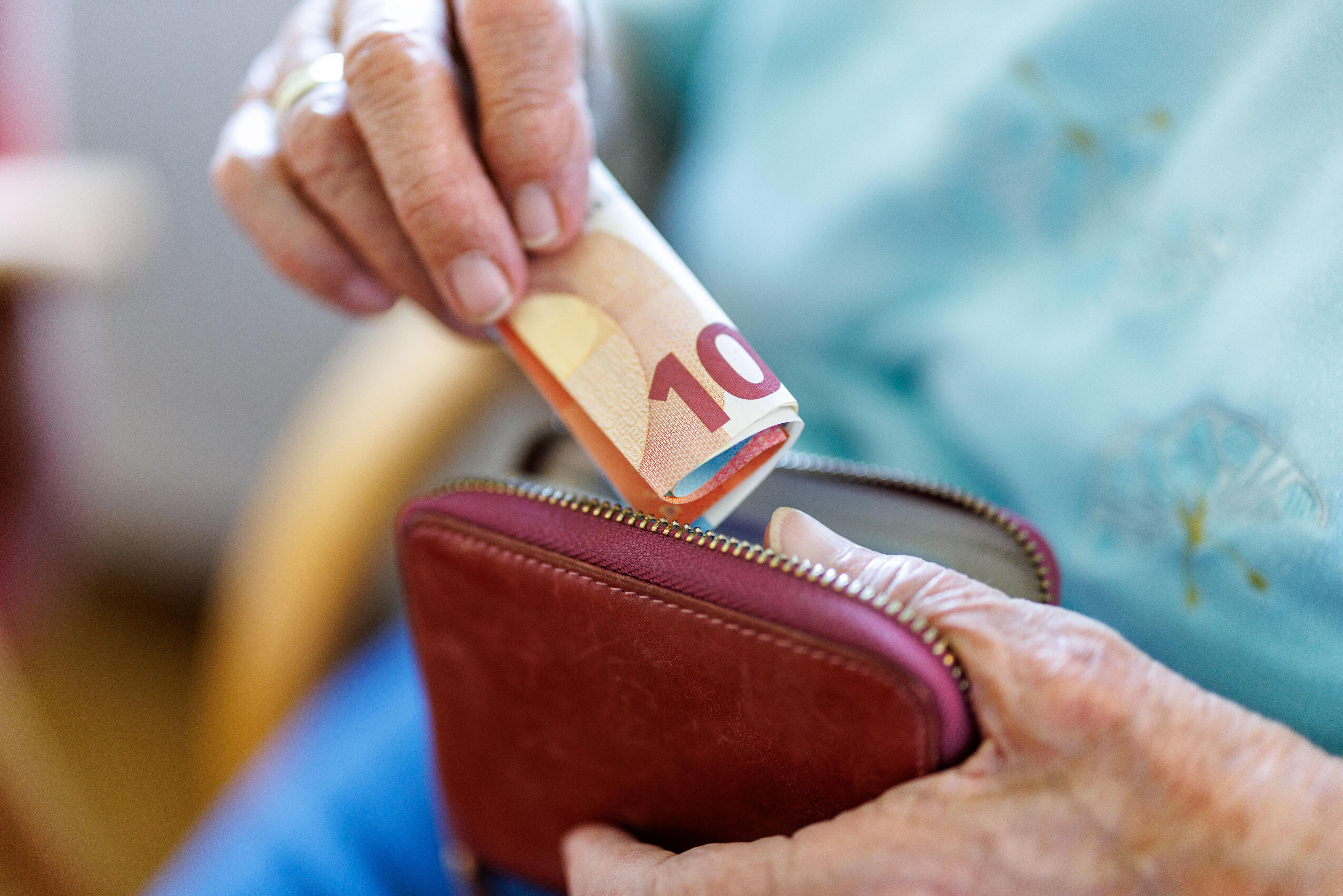 Eine 95-jährige Frau steckt ein Bündel von Geldscheinen in ihr Portemonnaie.
