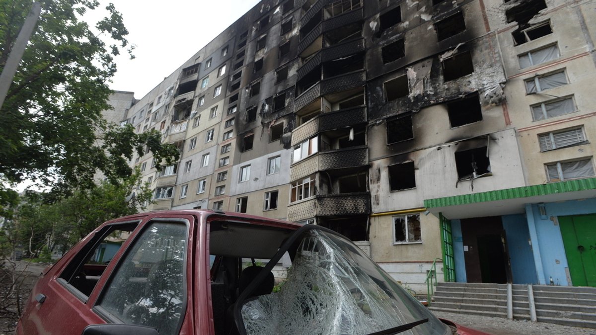 Charkiw: Ein zerstörtes Auto steht vor einem beschädigtem Gebäude.