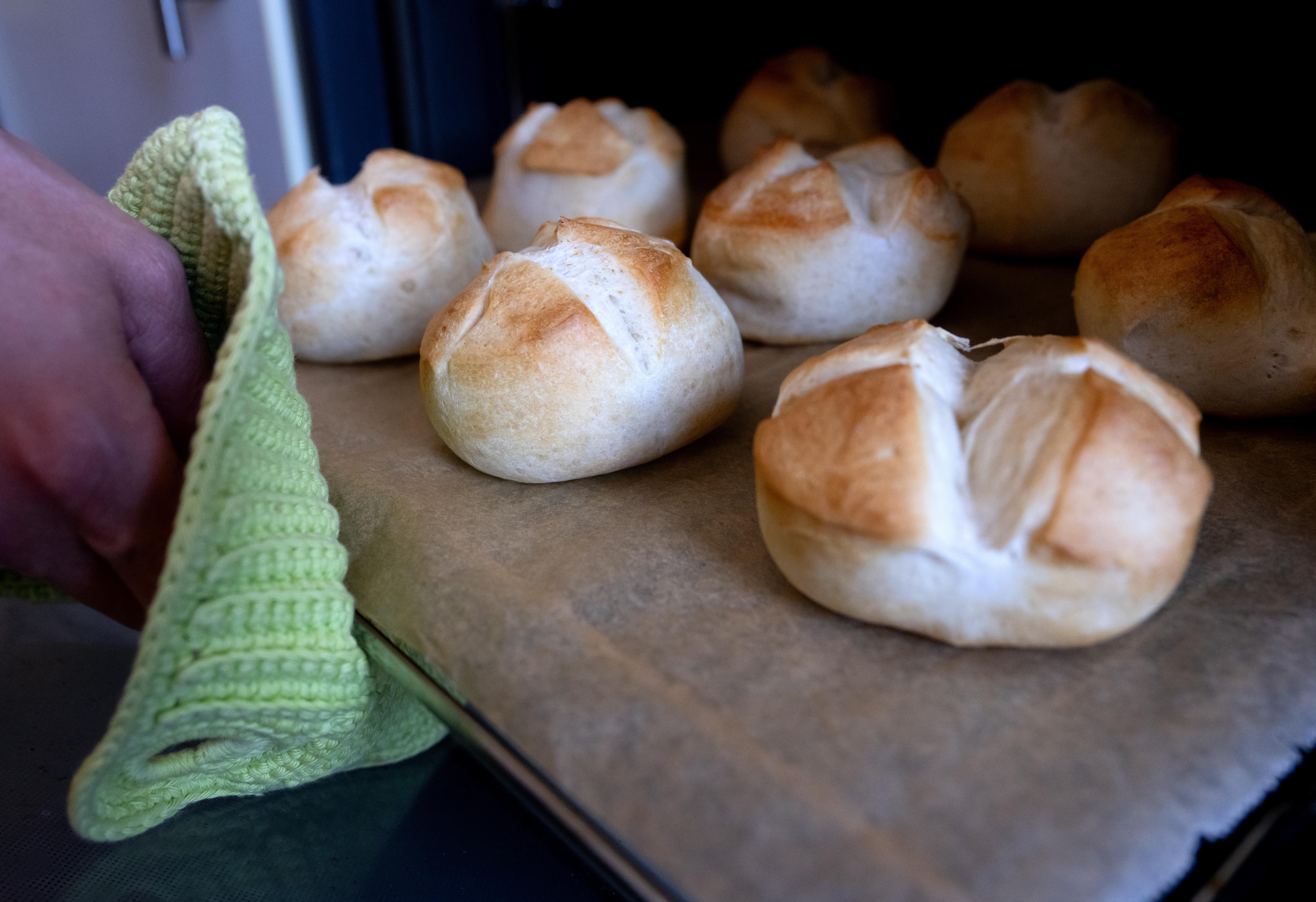 Eine Frau hält in einer Küche ein frisch gebackenes Aufbackbrötchen auf einem Ofenrost in der Hand. Einige Lebensmittel enthalten «versteckten» Alkohol - Verbraucherschützer fordern eine klarere Kennzeichnung.