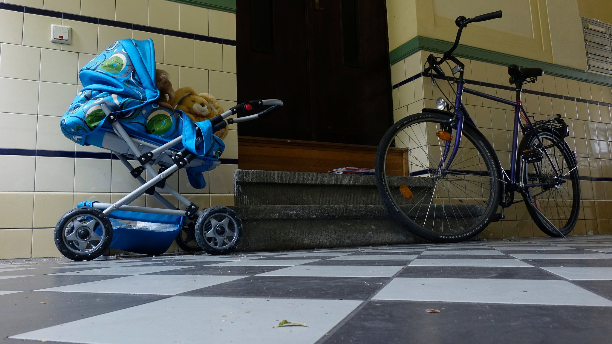 Ein Fahrrad und ein Kinderwagen sind in einem Hausflur abgestellt.