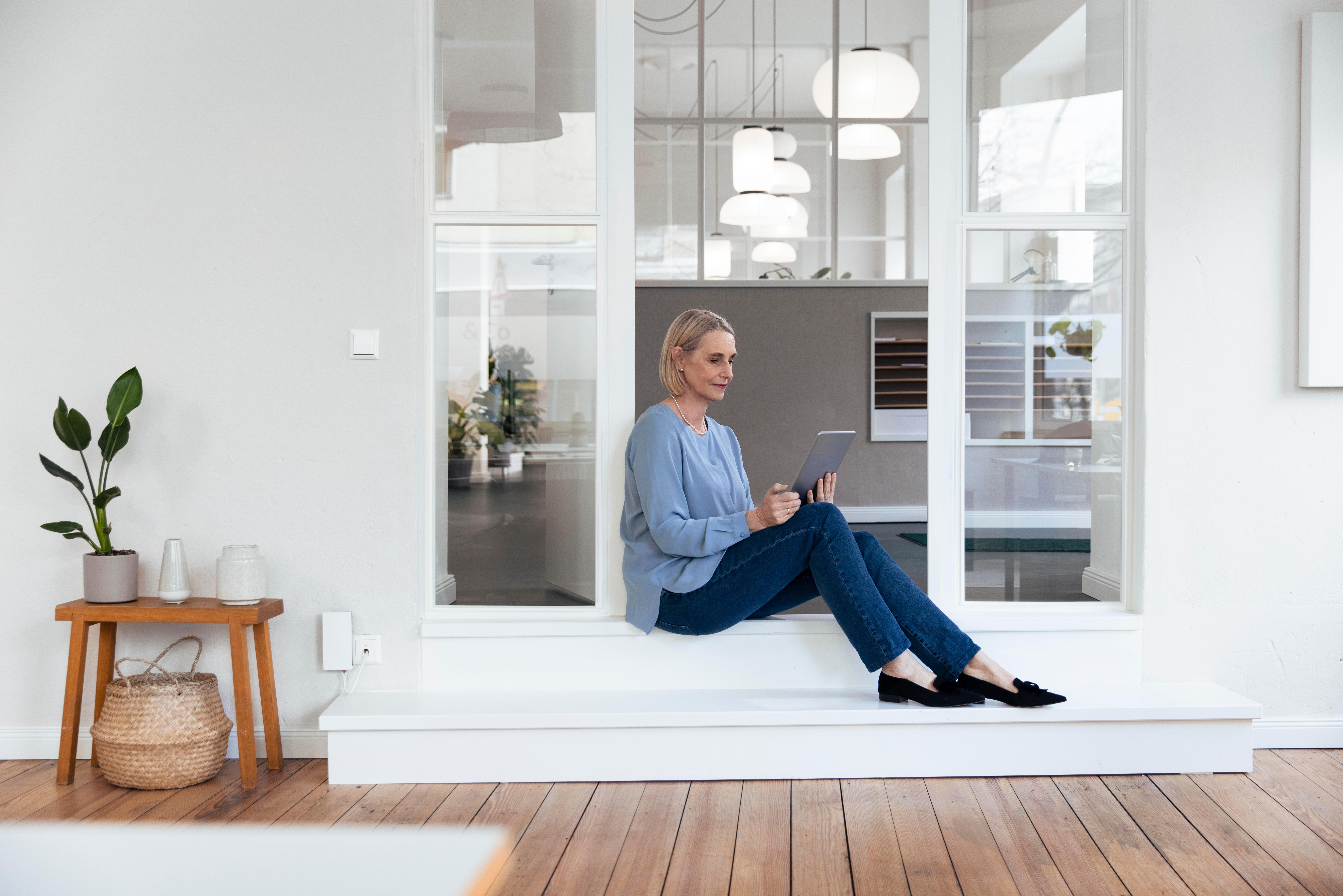 (Symbolbild) Frau sitzt mit ihrem Tablet am Boden und steuert ihre Geräte an