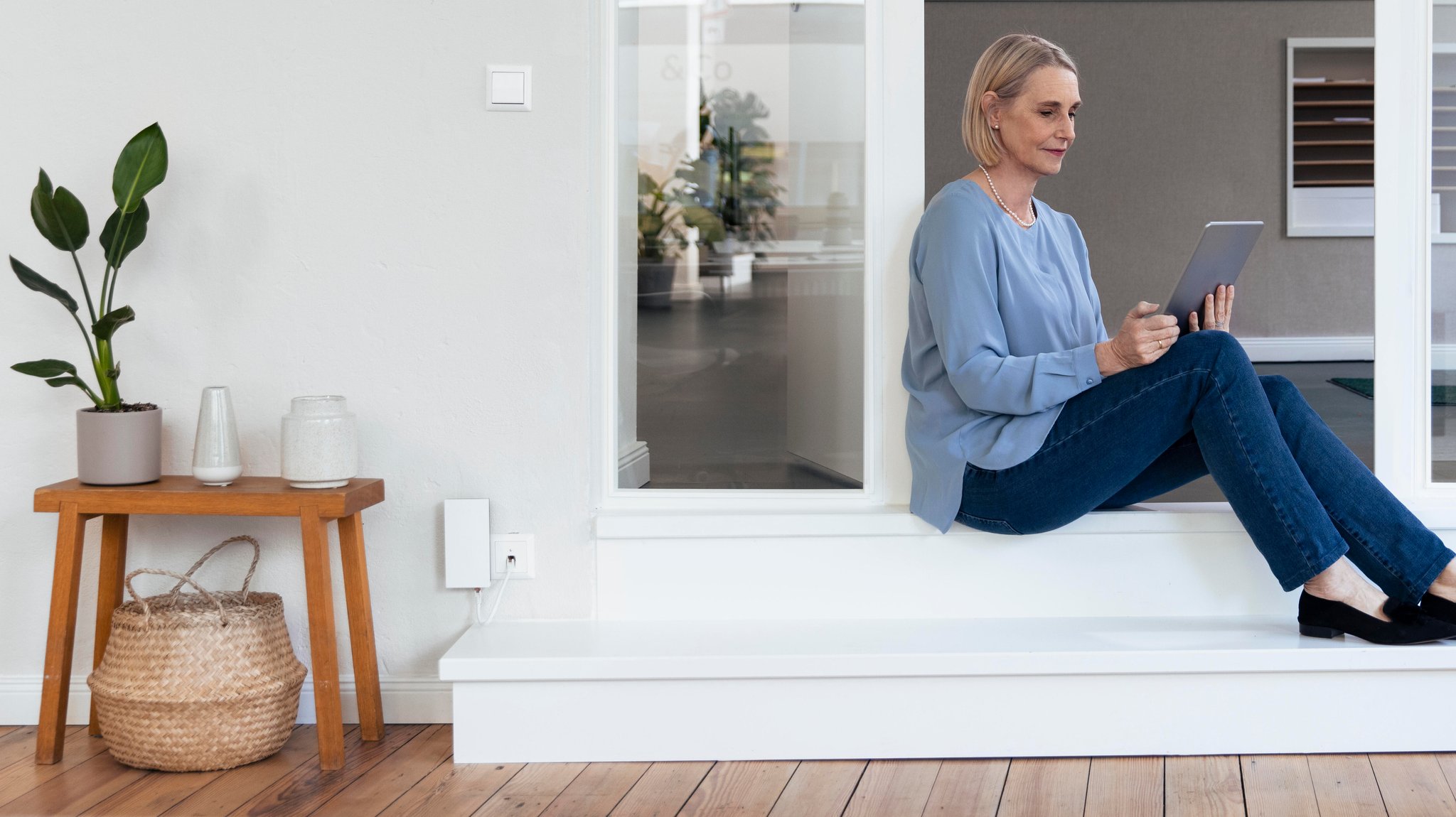 (Symbolbild) Frau sitzt mit ihrem Tablet am Boden und steuert ihre Geräte an
